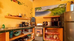 Eine kompakte Küche mit Herd, Backofen, Mikrowelle und Kühlschrank. Es gibt Regale mit Geschirr und einen Wasserspender.
