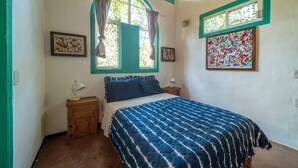 Ein Schlafzimmer mit einem Bett, zwei Nachttischen, einem Fenster mit Vorhängen und zwei an der Wand befestigten Bildern.