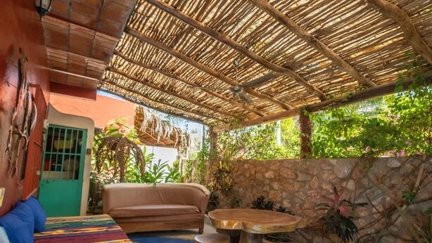 An outdoor patio with a thatched roof, a sofa, a round wooden table, and a small stool. - Casa Happy Sol - Delfin (San Francisco)