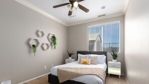 Une chambre à coucher avec un lit, un ventilateur de plafond, une fenêtre avec des stores et des décorations murales hexagonales.