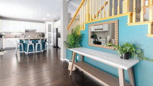Une cuisine moderne avec des meubles blancs, un coin bar avec des tabourets et un escalier en bois avec des rampes jaunes.