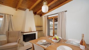 A dining area with a wooden table set for four, a fireplace, and a view through a glass door. - Elida Inn (Markopoulo Mesogaias)
