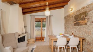 A cozy dining area with a wooden table set for two, a sofa, and a stone wall with a painting. - Elida Inn (Markopoulo Mesogaias)