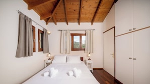 A bedroom with a wooden ceiling, a bed with white linens, two bedside tables with lamps, and a wardrobe. - Elida Inn (Markopoulo Mesogaias)