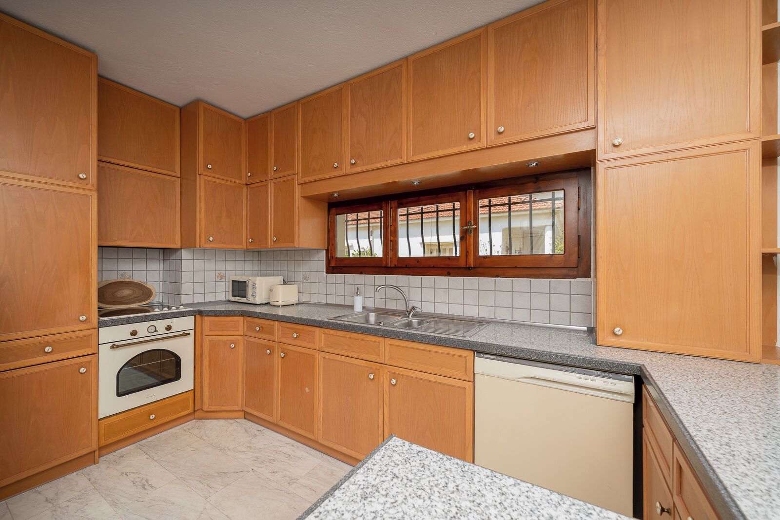A kitchen with wooden cabinets, a built-in oven, a dishwasher, and a window with a view of the outside.