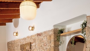 A living room with a stone wall, a round mirror, a gray sofa, and a wooden coffee table. - Elida Inn (Markopoulo Mesogaias)
