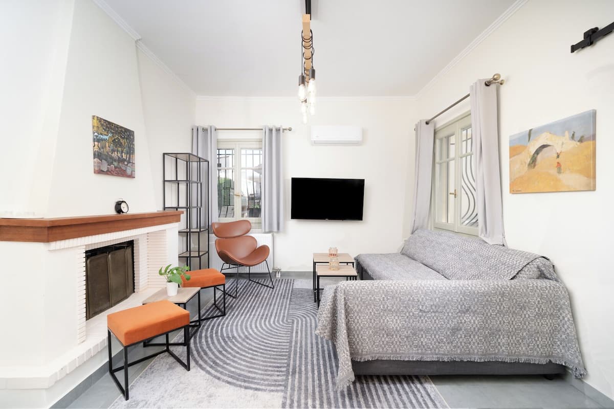 A modern bedroom with a fireplace, a sofa, a chair, a TV, and artwork on the walls.