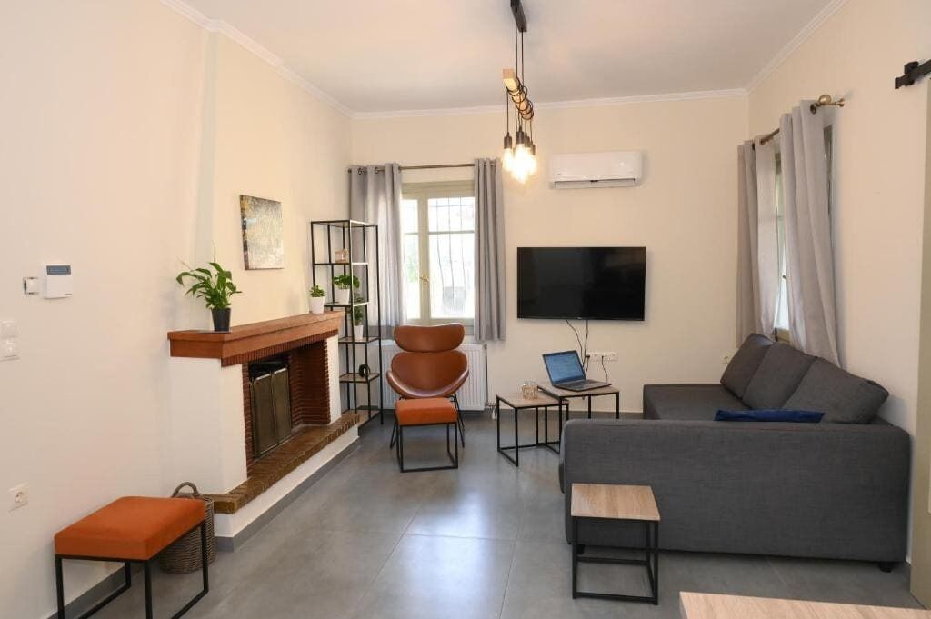 A modern living room with a fireplace, a grey sofa, a TV, and a laptop on a small table.