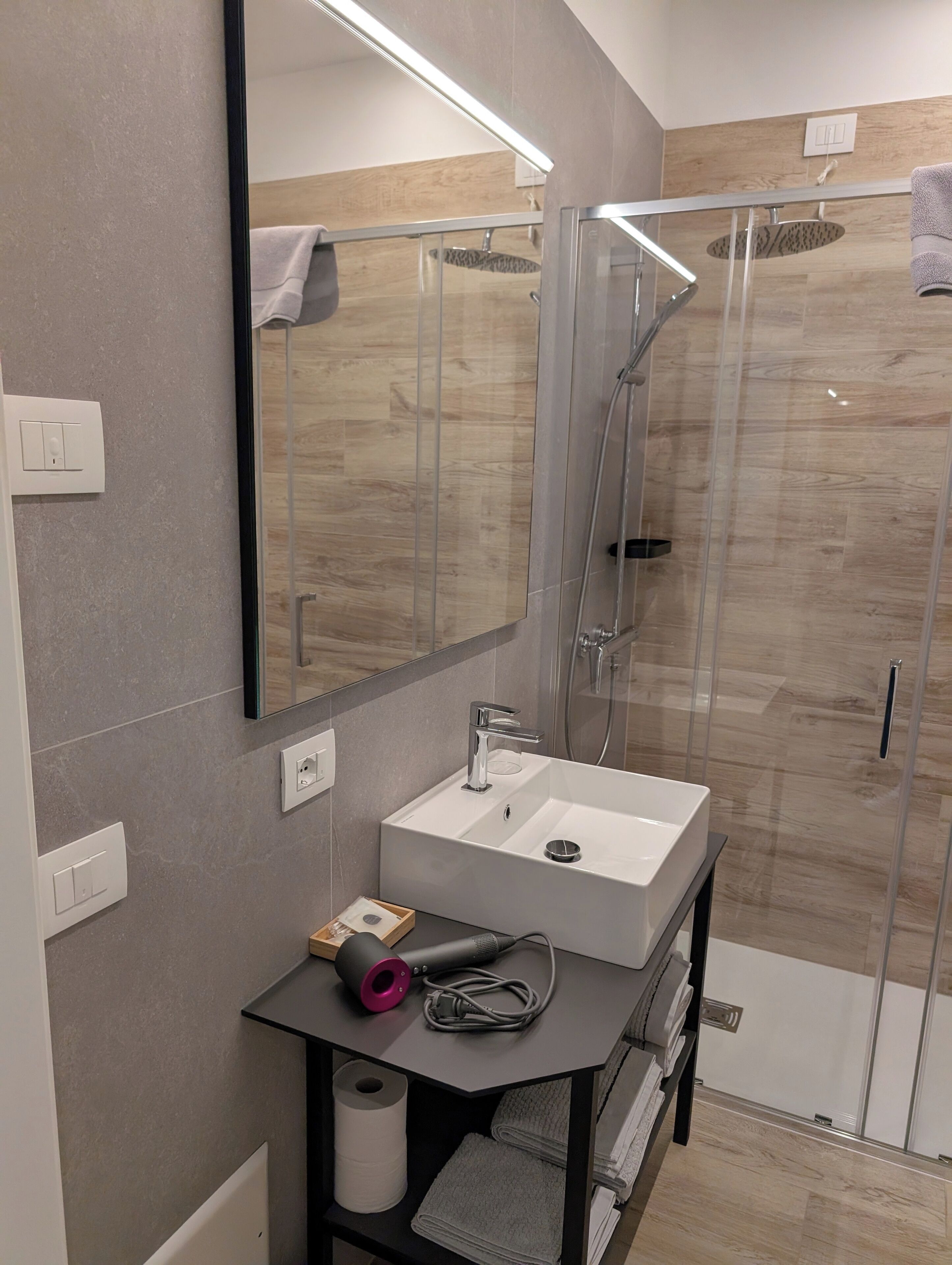 Ein modernes Badezimmer mit einer in Glas eingefassten Dusche, einem weißen Waschbecken und einem Spiegel darüber.