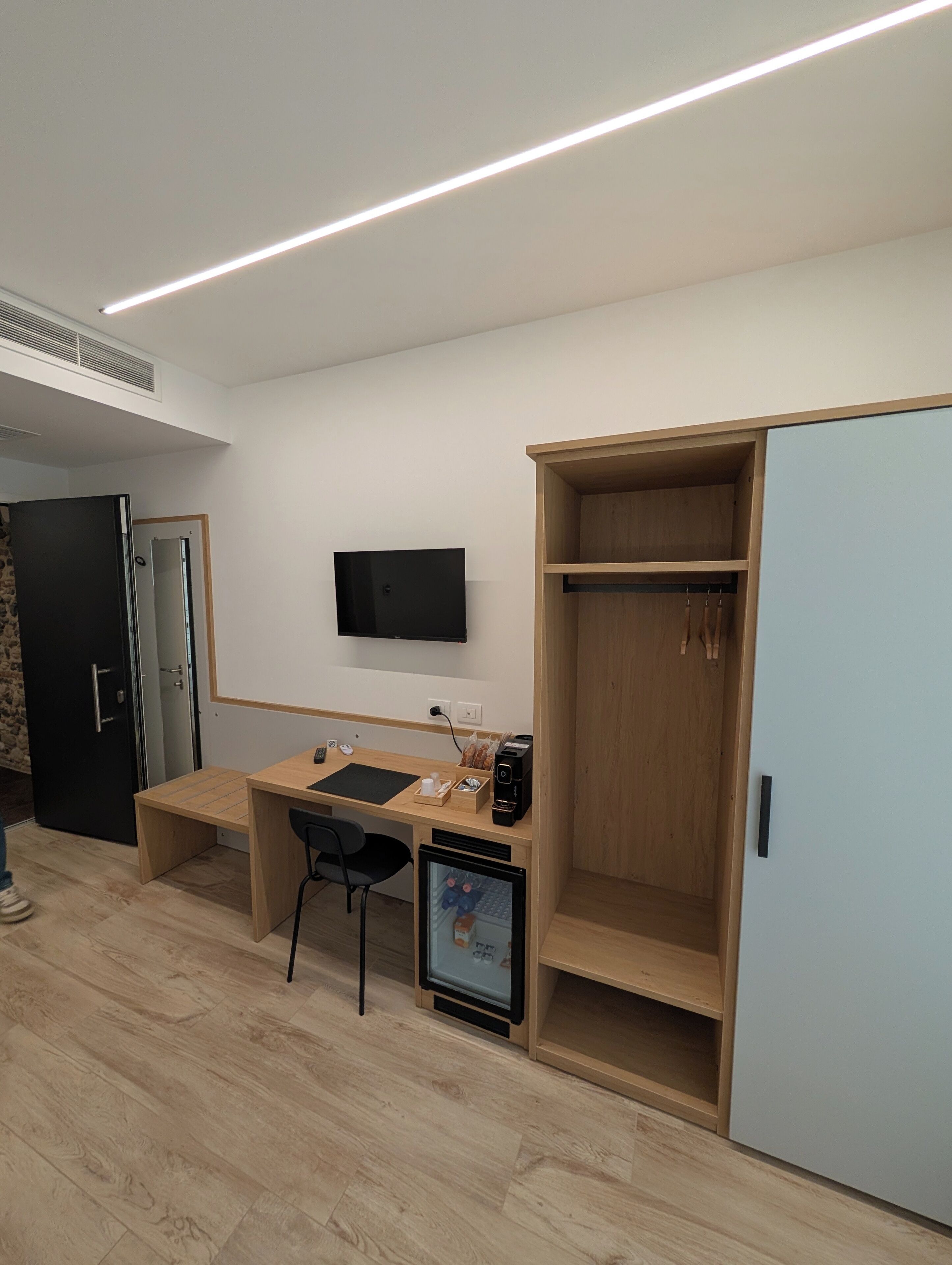A modern room with a wooden desk, a black chair, a TV mounted on the wall, and a wardrobe with a mirror.