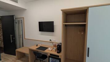 Una habitación moderna con un escritorio de madera, una silla negra, un televisor montado en la pared y un armario con espejo.