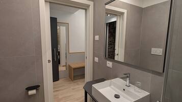 A modern bathroom with a white sink, a large mirror, and a wooden bench in the background.