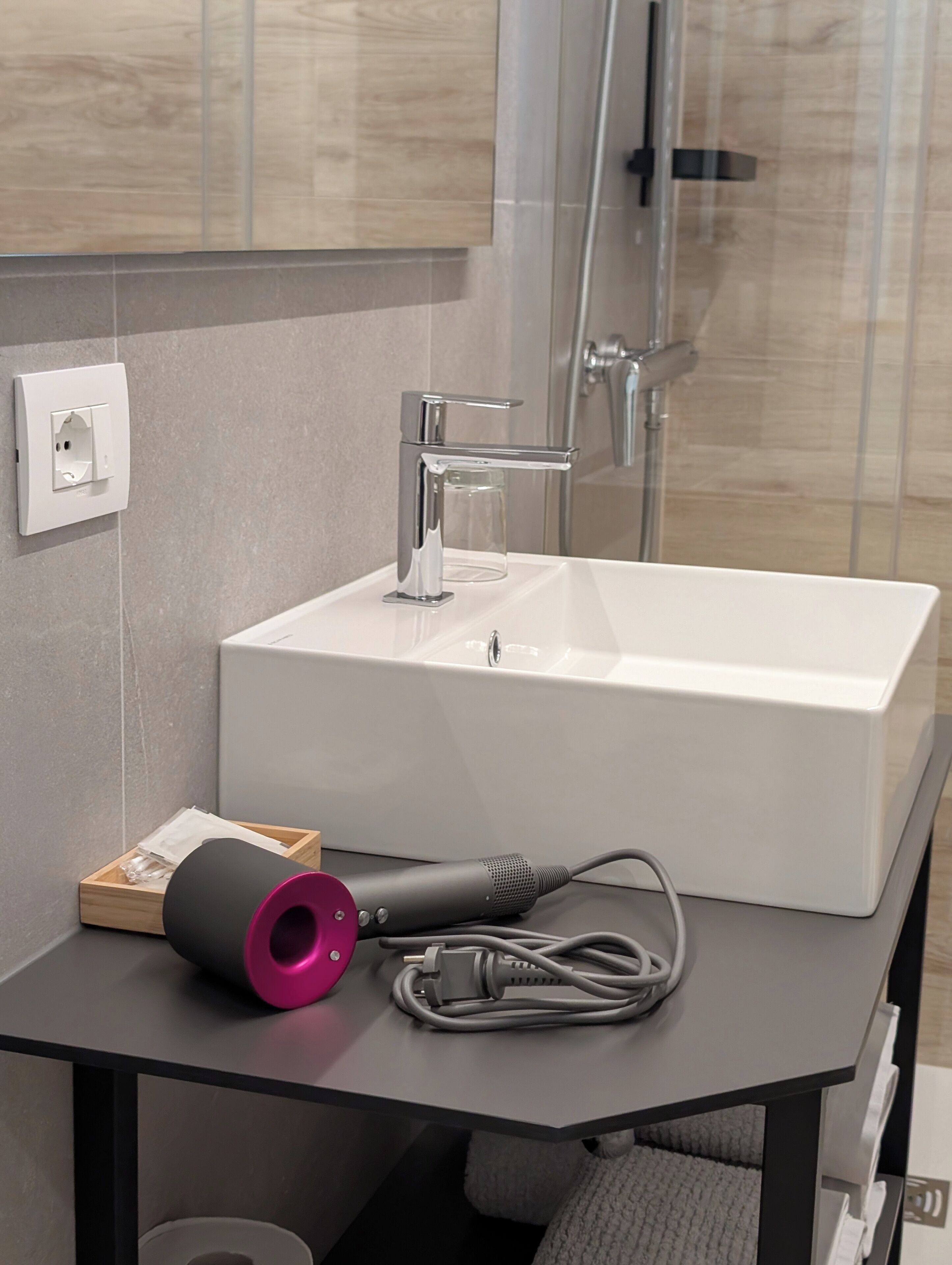 Ein modernes Badezimmer mit einem weißen Waschbecken, einem Föhn und einer Duschkabine.