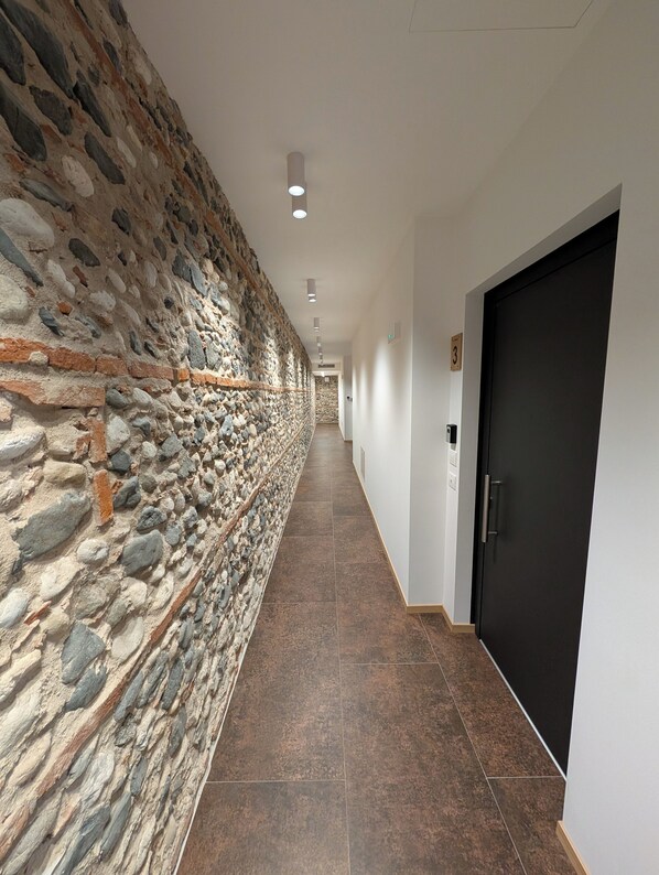 Un pasillo con pared de piedra, una puerta negra y un cartel con el número 3.
