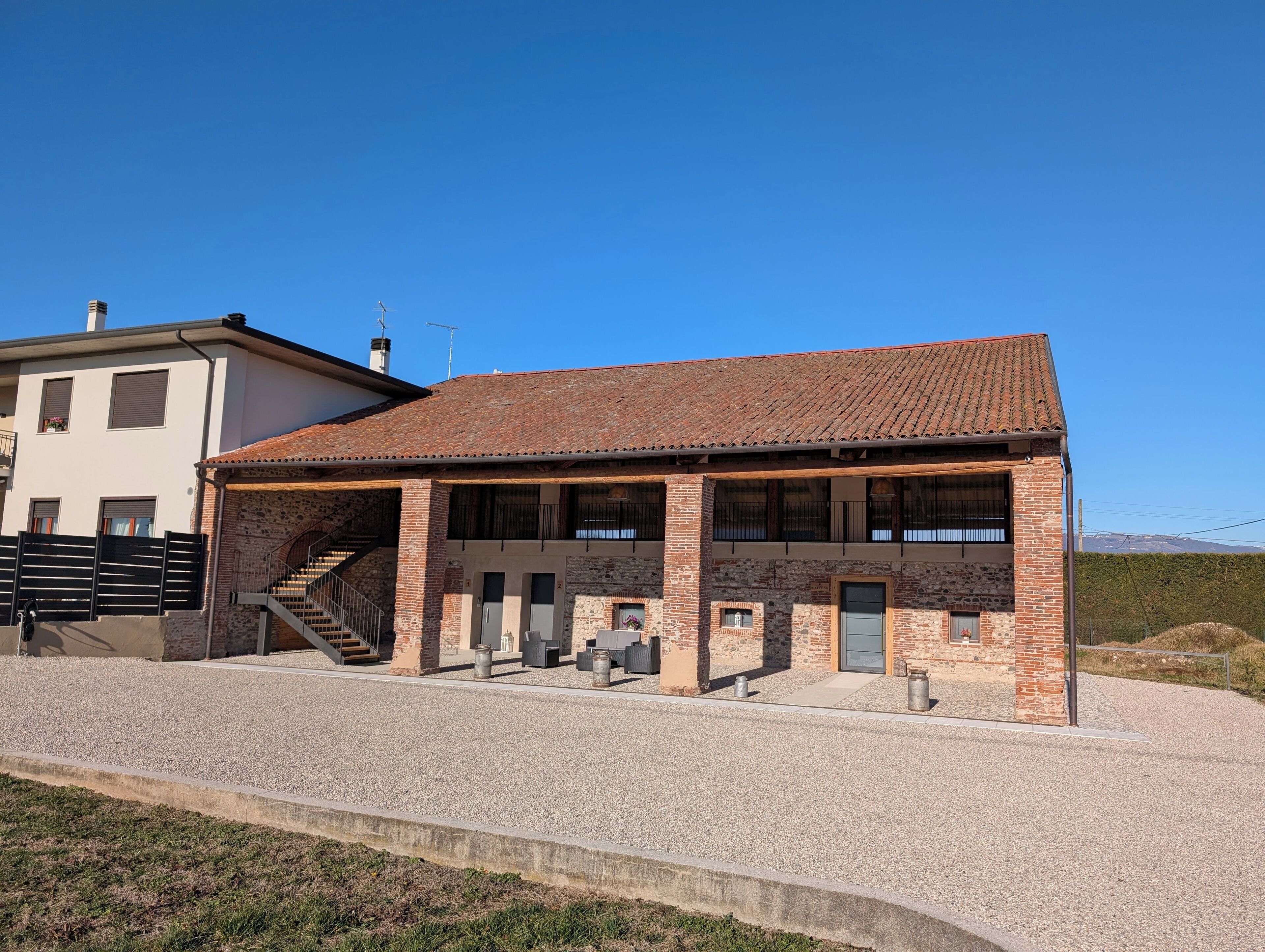 A two-story building with a tiled roof, a stone facade, and a gravel driveway.