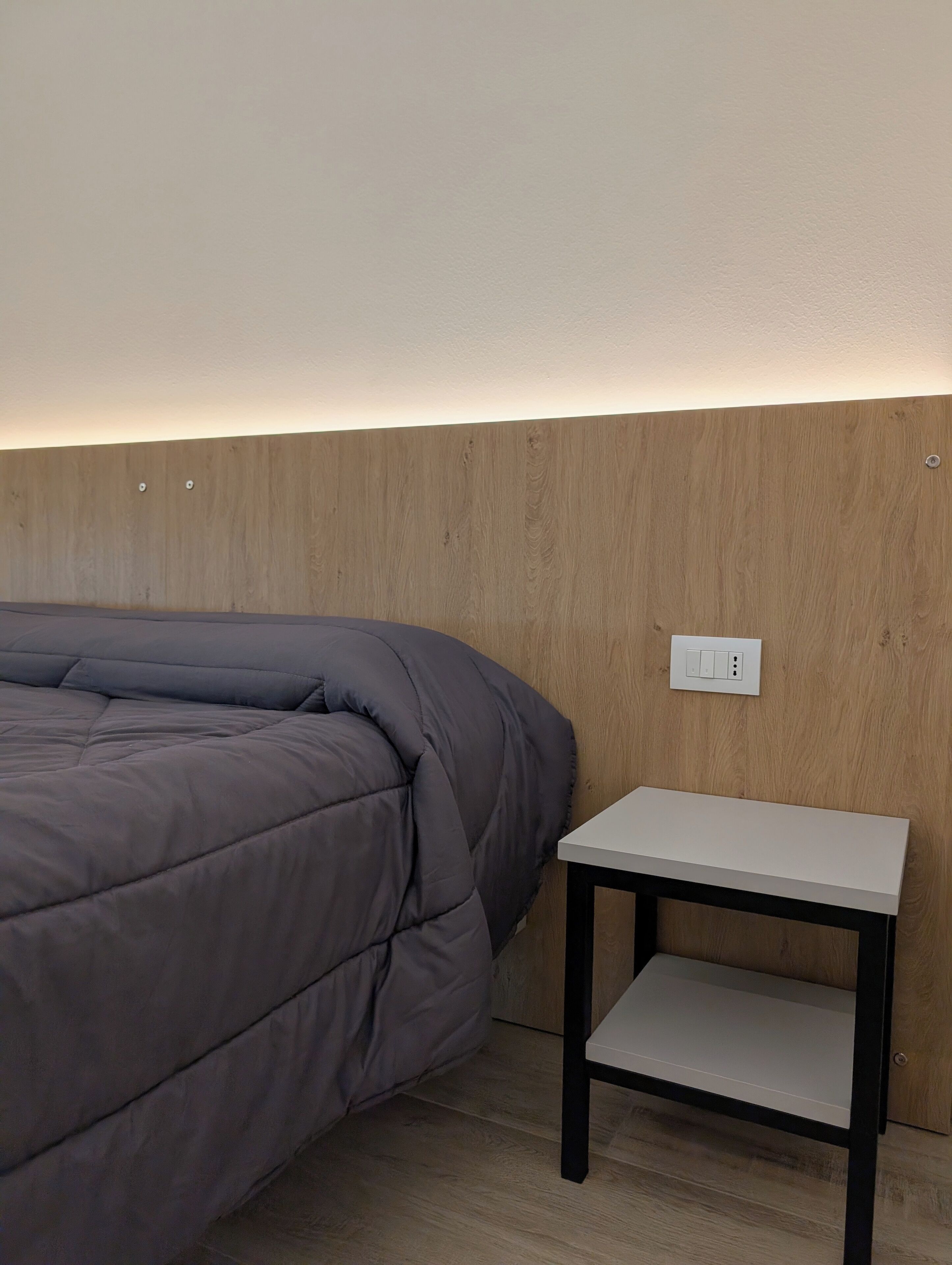 Une chambre moderne avec un lit, une table de chevet et un interrupteur fixé au mur.