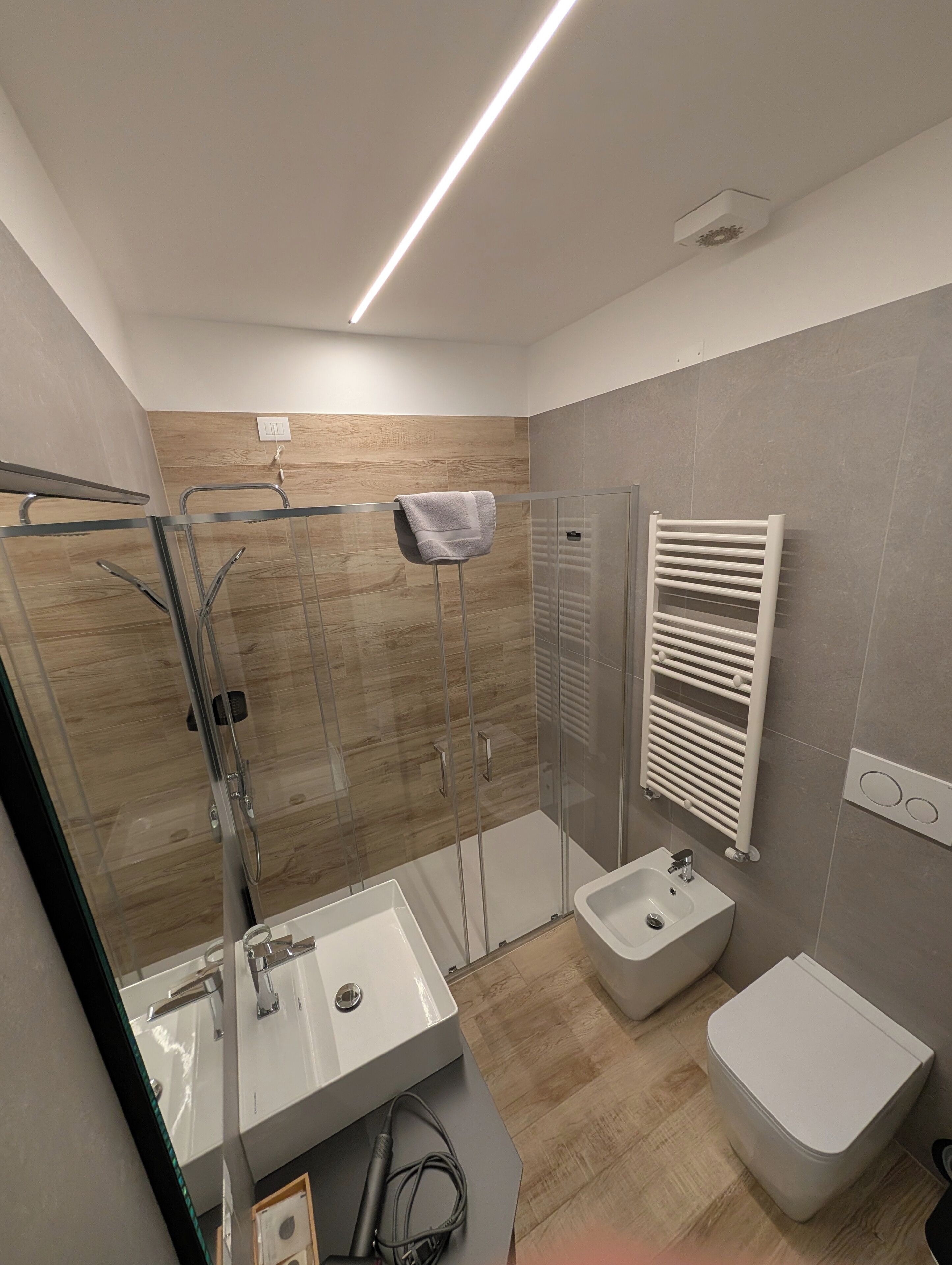 Un bagno moderno con doccia vetrata, lavandino bianco, bidet e porta asciugamani.