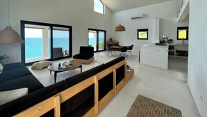 Een ruime woonkamer met een groot raam met uitzicht op zee, een houten bank en een eethoek met panorama.