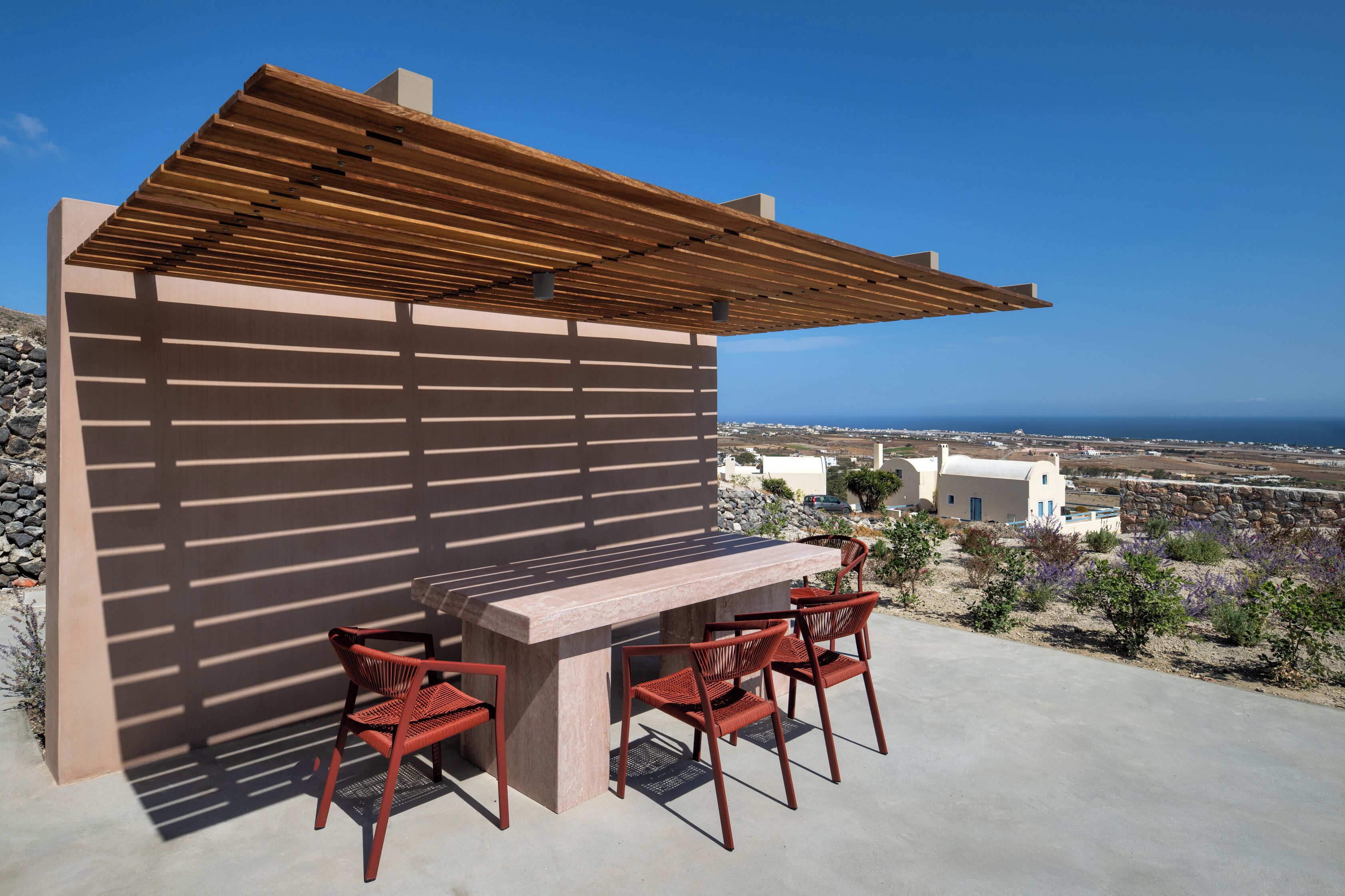 Un patio al aire libre con una pérgola de madera, una mesa de piedra y sillas rojas.