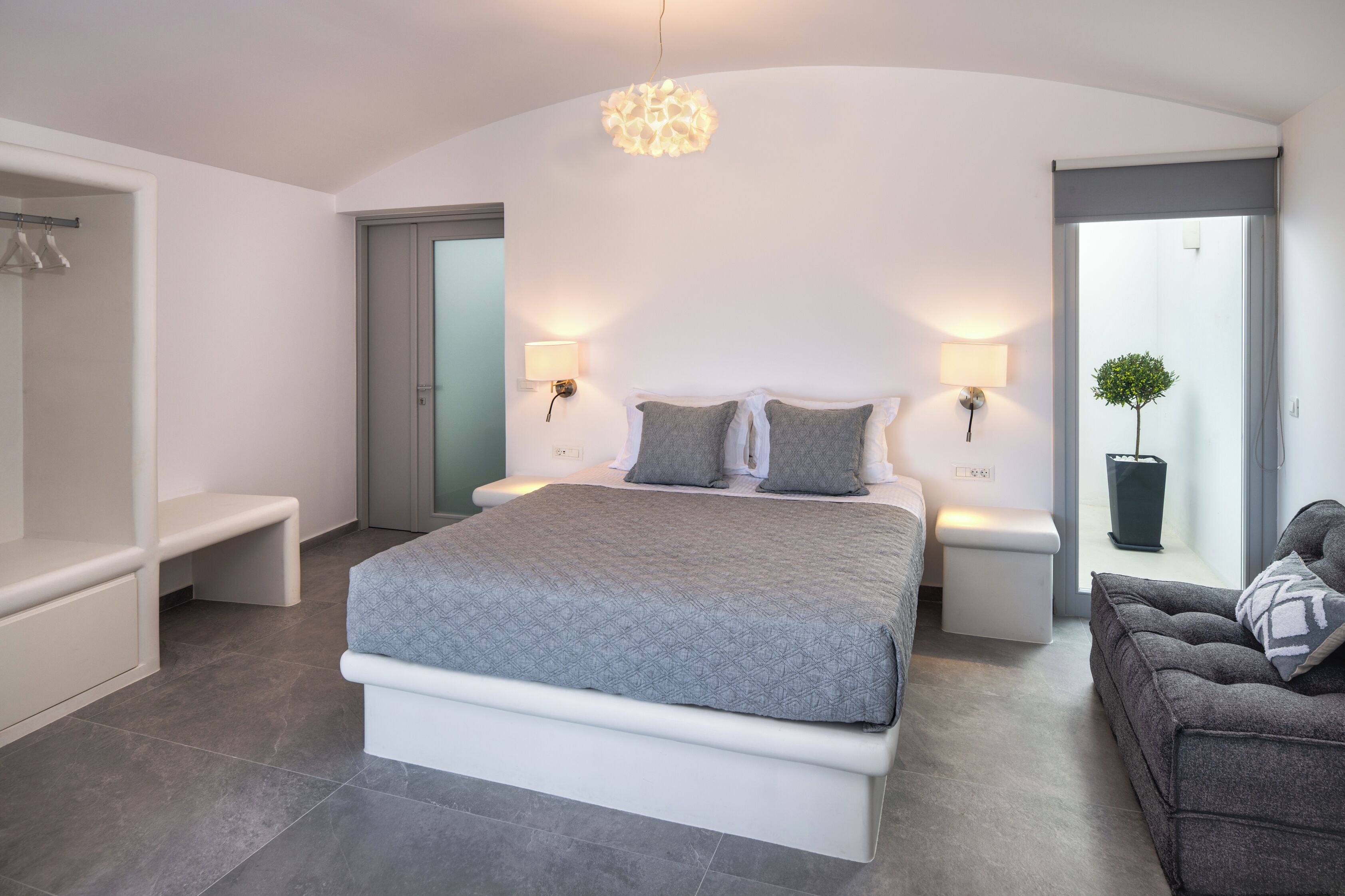 Une chambre à coucher moderne avec un grand lit, des lampes de chevet, un canapé gris et une plante en pot.