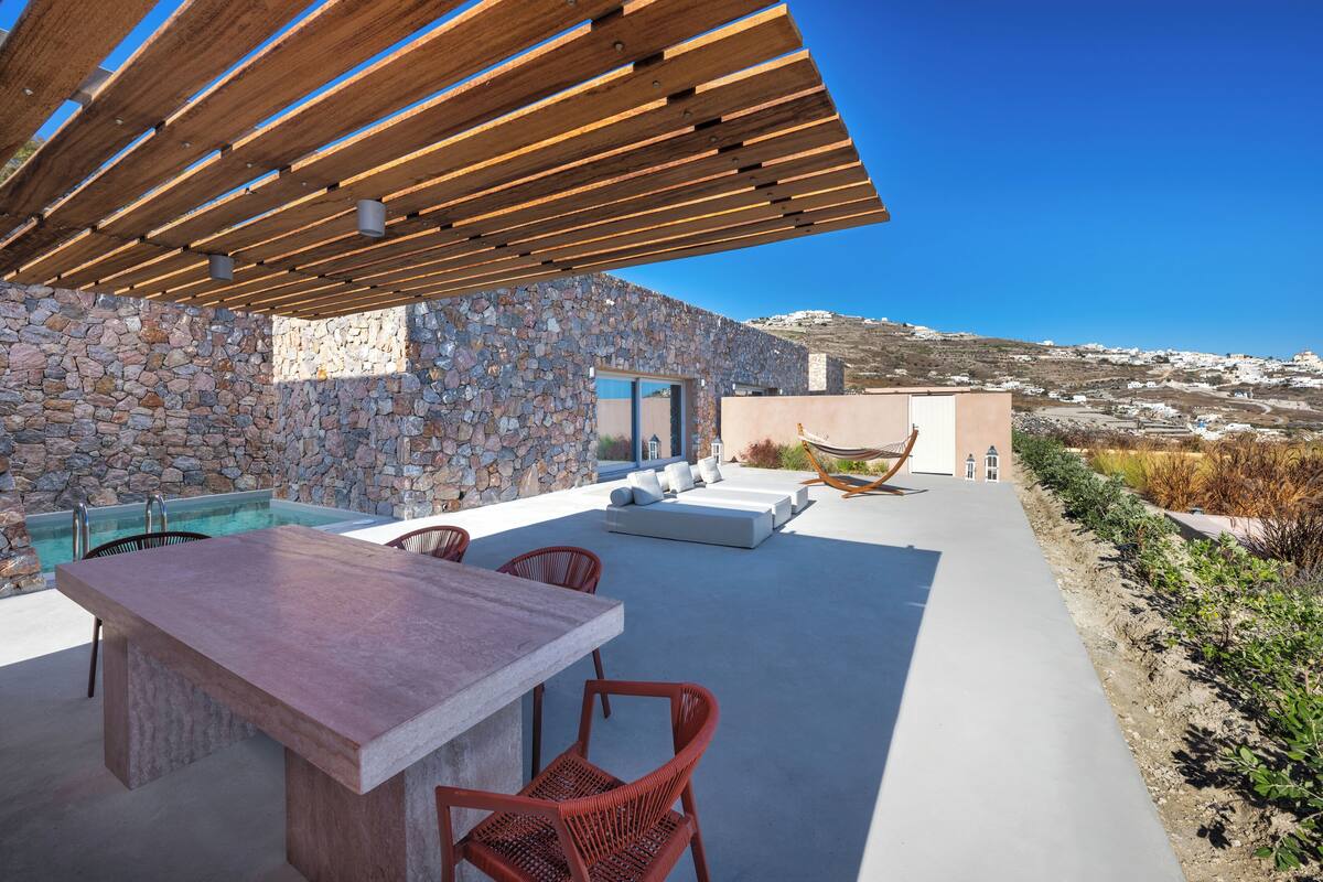 Eine Terrasse im Freien mit einer Steinmauer, einem Pool, einer Holz-Pergola und Blick auf die Landschaft.