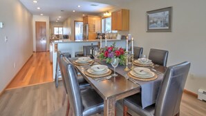 A dining area with a long table set for six, surrounded by chairs. There is a kitchen in the background with wooden cabinets and a refrigerator. - Hot Tub with Amazing Views, Game Room, Family Friendly, Central Location (Glenwood Springs)