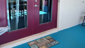 Una porta rossa con pannelli di vetro, un pavimento blu e un tappetino d'ingresso a tema spiaggia.