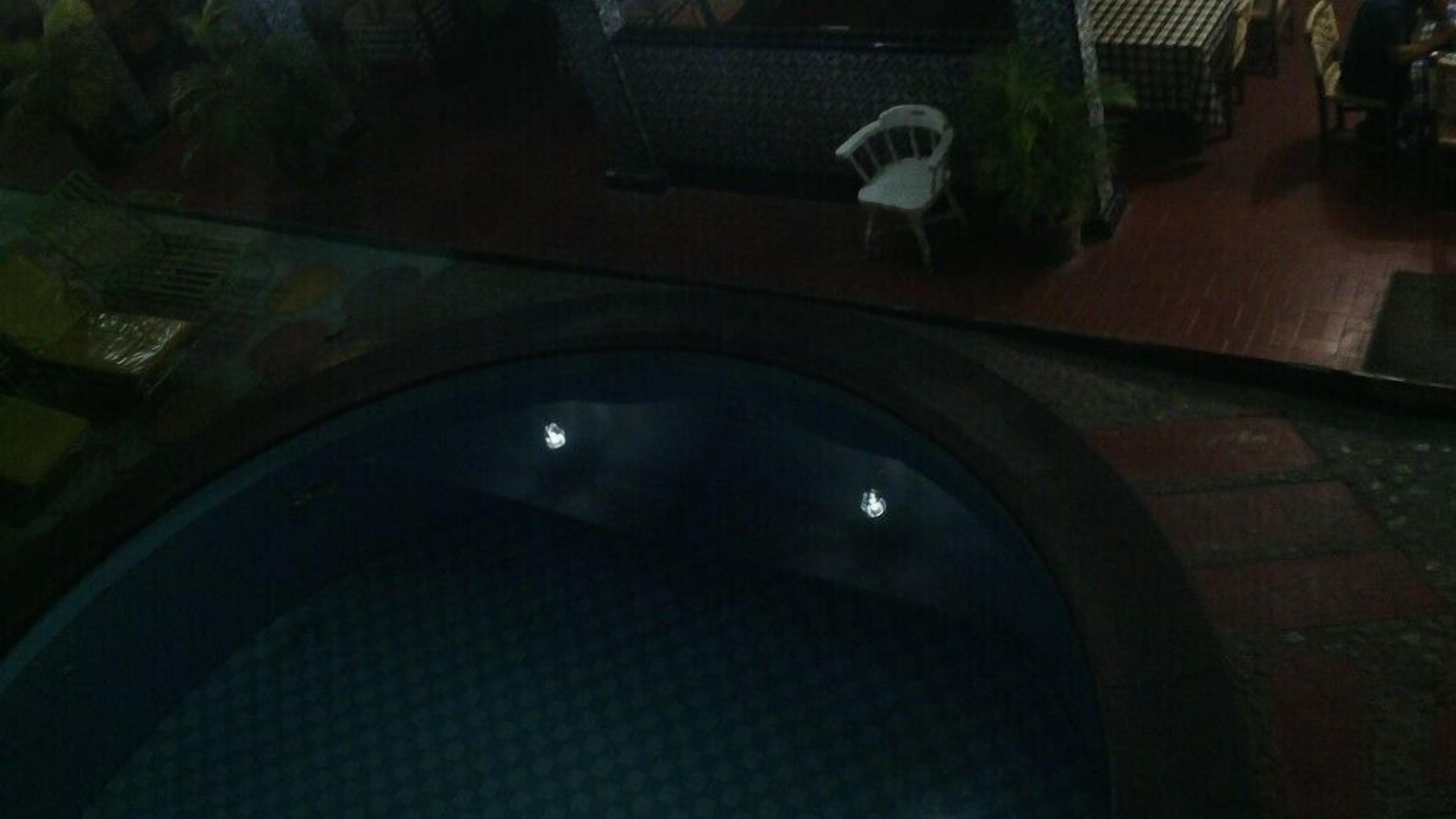 A dimly lit indoor pool area with a circular pool, a white chair, and a tiled floor.