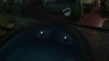 A dimly lit indoor pool area with a circular pool, a white chair, and a tiled floor.