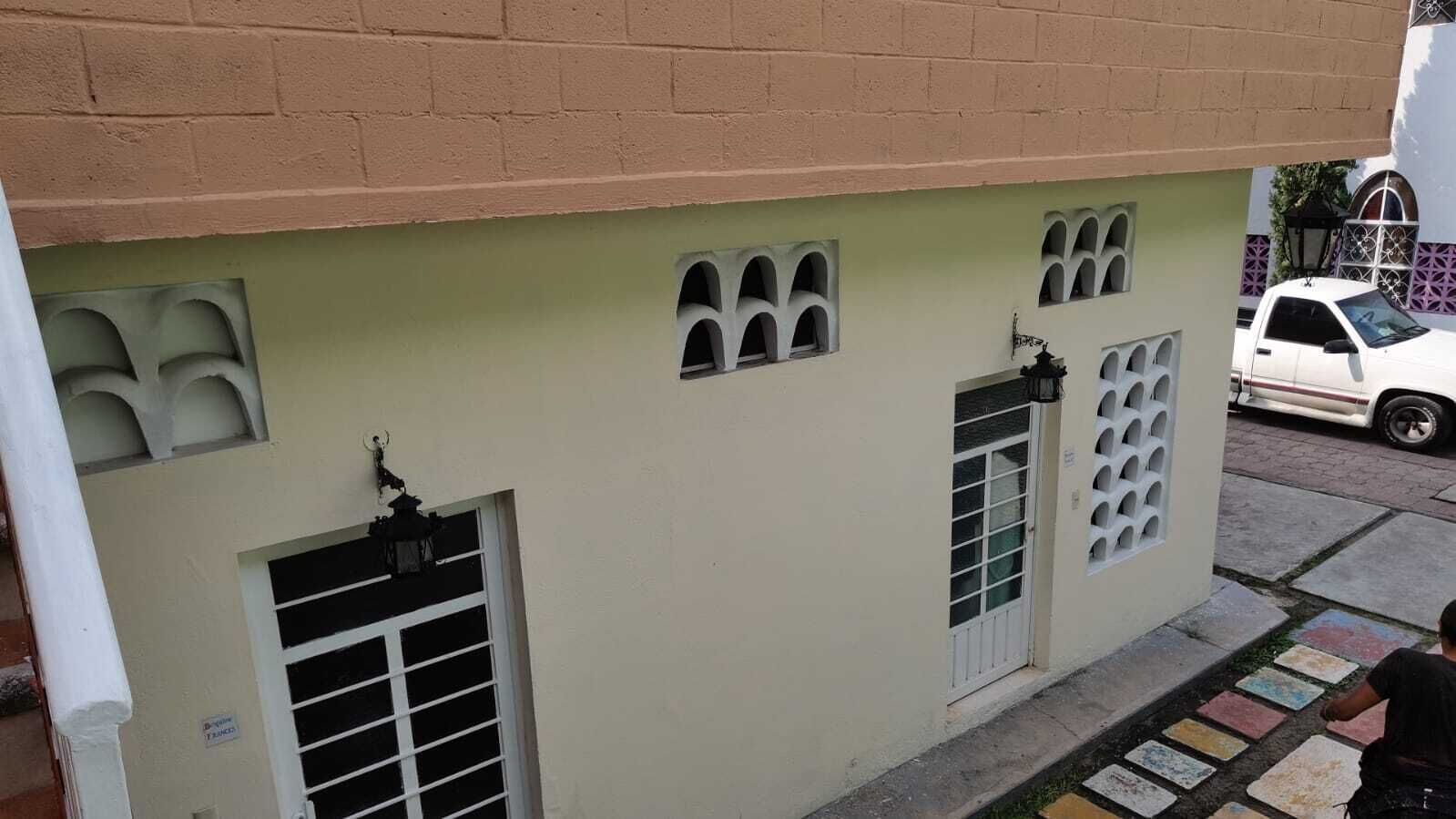 Un edificio con fachada color beige, varias ventanas y un vehículo blanco estacionado cerca.