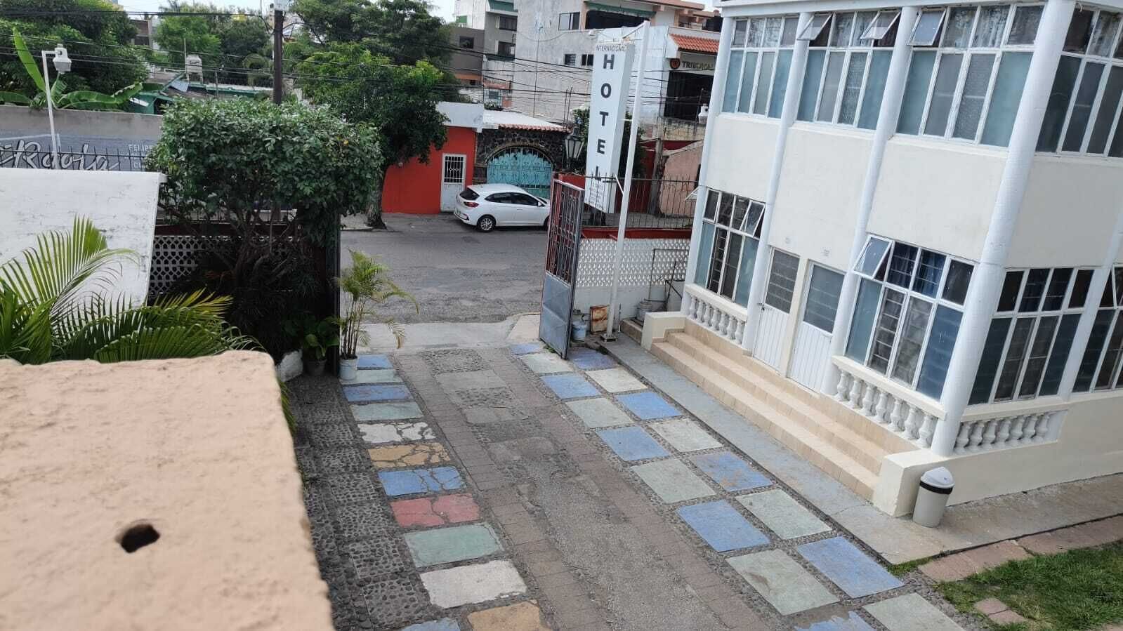 Una entrada de hotel con un coche blanco estacionado frente, un camino con puerta y una escalera que conduce a la entrada.