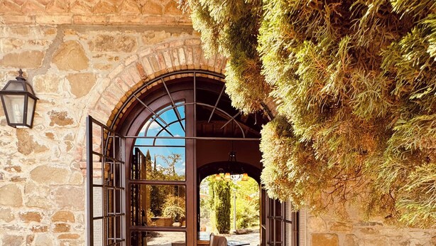An open wooden door leading to a stone-walled interior with a view of a garden.