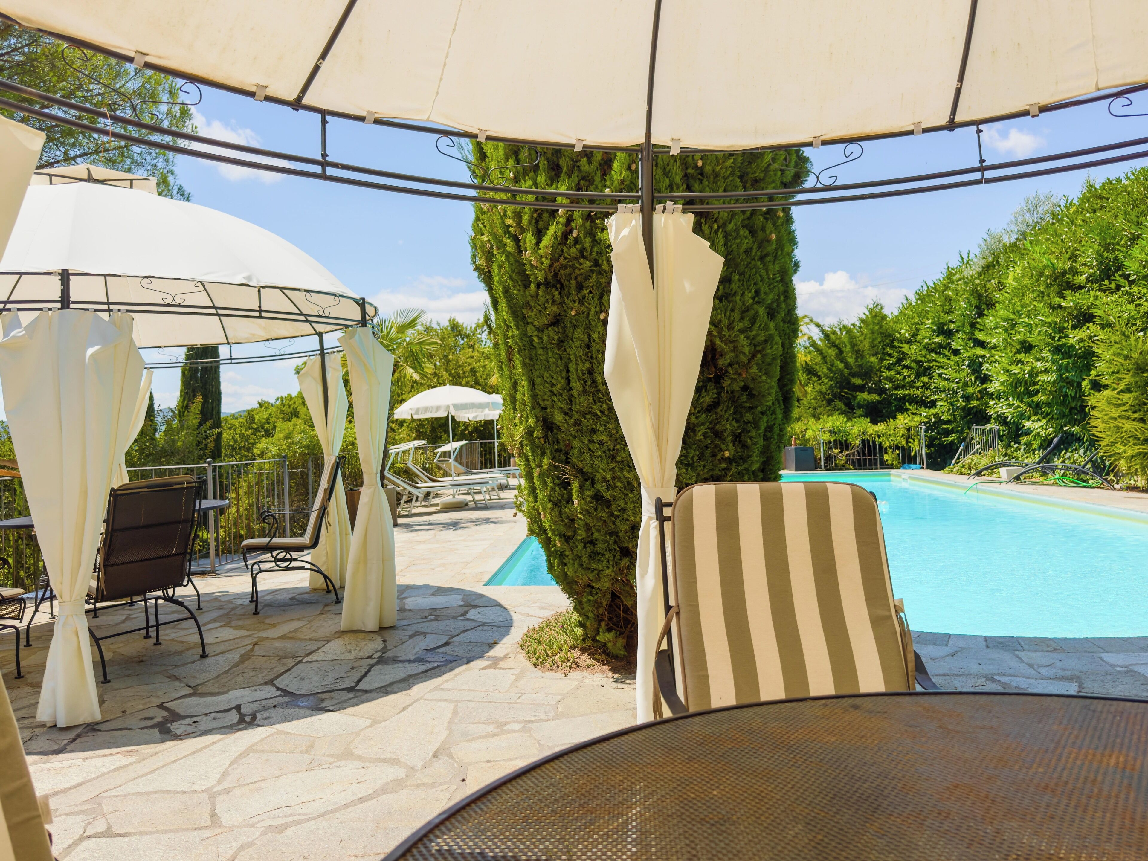 Area piscina con lettini, ombrelloni e terrazza in pietra.