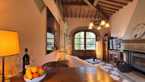 A cozy dining area with a wooden table, a bowl of fruit, wine glasses, and a fireplace.