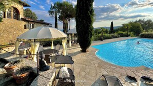 A pool area with a stone patio, outdoor seating, and a view of the pool.