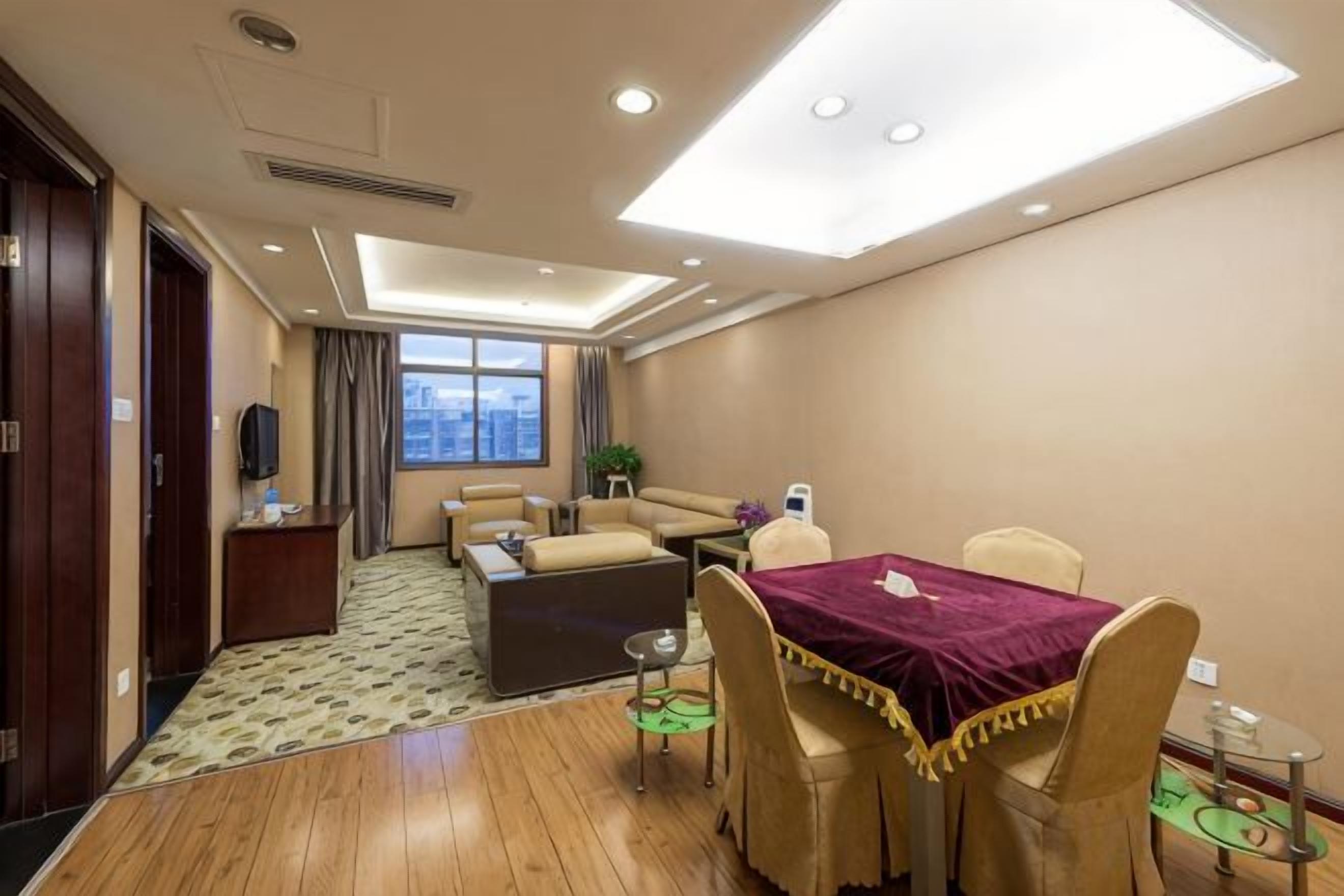 A hotel room with a dining area, a sofa, a TV, and a window with a city view.