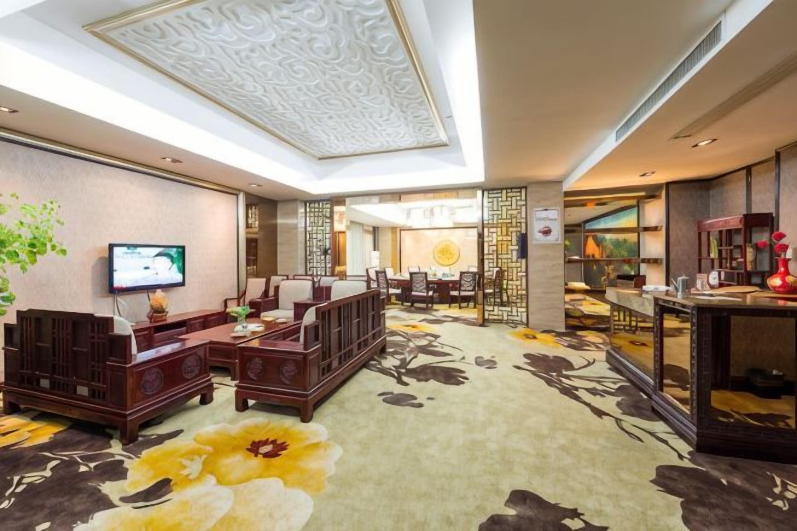 A hotel lobby with a sofa set, a television, a dining area, and a reception desk.