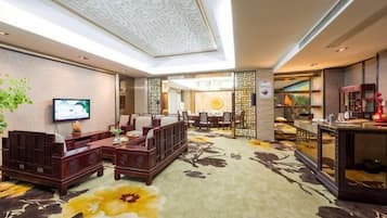 A hotel lobby with a sofa set, a television, a dining area, and a reception desk.