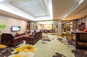 Un hall de hotel con un conjunto de sofás, un televisor, un comedor y un mostrador de recepción.