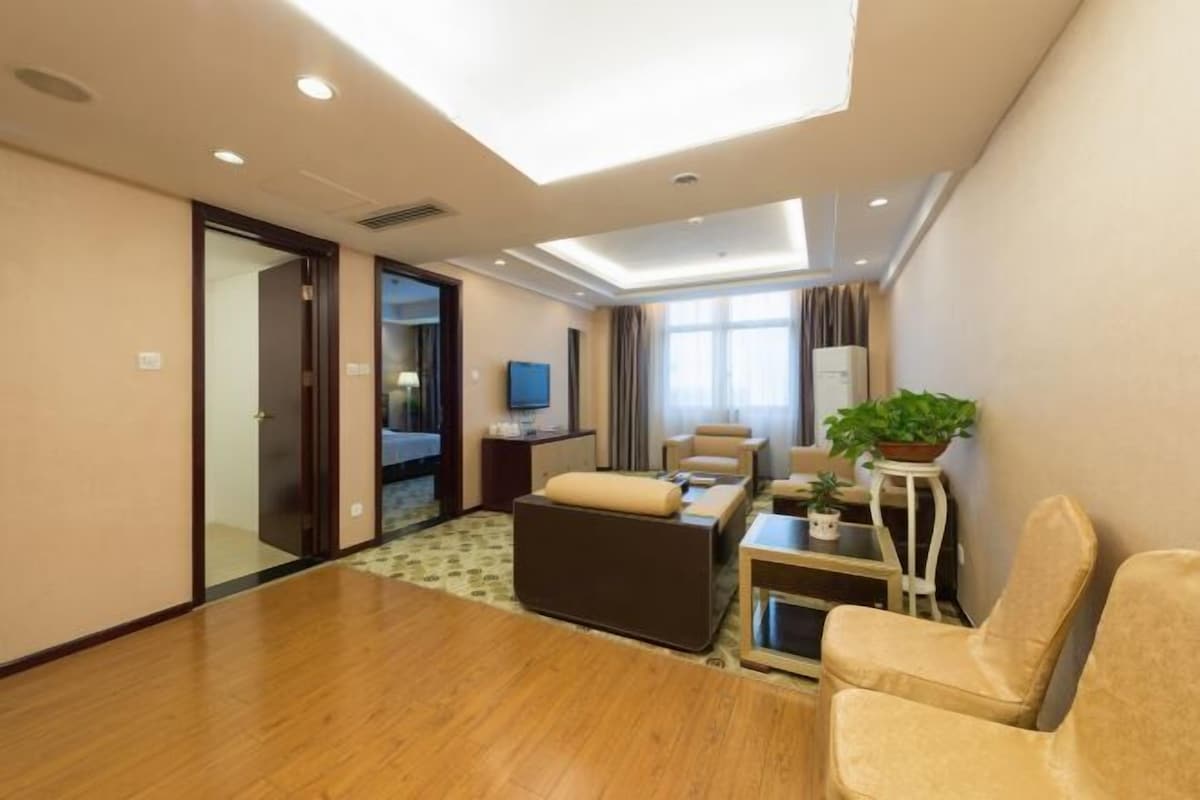 Habitación de hotel con piso de madera, un sofá, una mesita, un televisor y una planta en maceta.