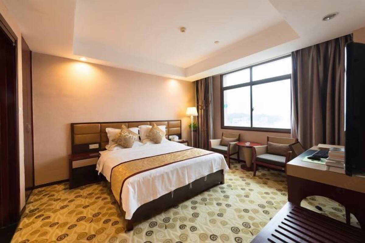 A hotel room with a large bed, a desk, a chair, a TV, and a window with curtains.