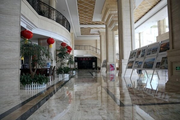 A spacious lobby with marble flooring, a curved wall, and a balcony with red lanterns.
