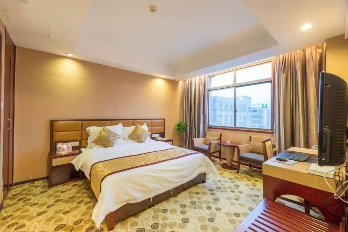 A hotel room with a large bed, a desk with a computer, a chair, and a small table.