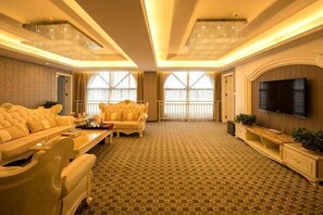 A spacious living room with a patterned carpet, a large flat-screen TV, and a balcony with a railing. - Gan Jiang Yuan International Hotel (Shicheng)