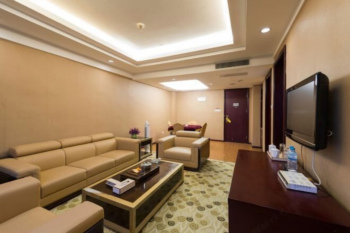 Una habitación de hotel con sofá, sillones, una mesa de centro, televisor y una puerta.