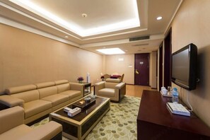 Una habitación de hotel con sofá, sillones, una mesa de centro, televisor y una puerta.