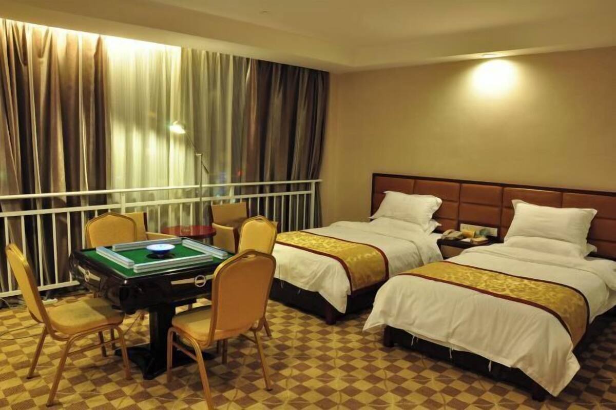 A hotel room with two beds, a table with a board game, and a view of the outside through curtains.