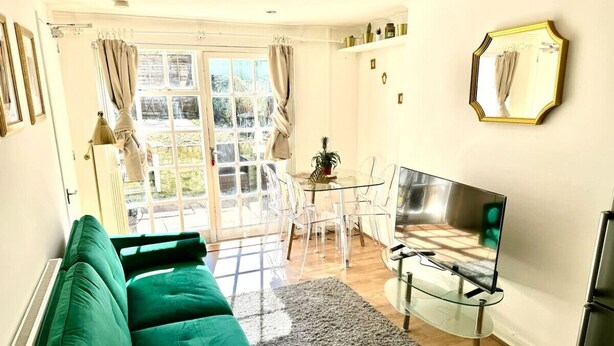 A living room with a green sofa, a glass coffee table, a flat-screen TV, and a dining area with clear chairs. - Modern 2BR Garden Flat King’s Cross - London (Greater London)