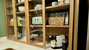 Une cuisine avec des meubles en bois, un plan de travail en marbre et divers ustensiles, comme une machine à café et des bocaux.