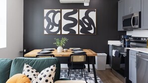 Una cocina moderna con comedor, que presenta una pared negra con arte abstracto, un aire acondicionado blanco y un microondas de acero inoxidable.